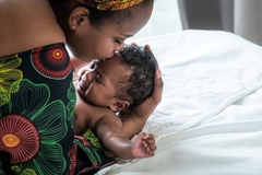 Image A Nigerian woman kisses her baby on the bed.