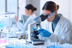 Image A female scientist looking into a microscope.