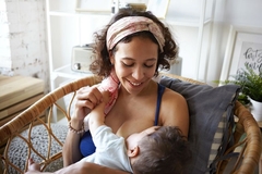 Image A woman smiles down at her baby while breastfeeding in wicker chair.