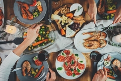Image Several people sitting around a table filled with Mediterranean diet foods, including fish and vegetables.