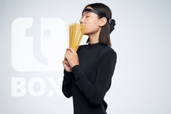 Image a woman in a black dress smelling raw pasta wearing a headset