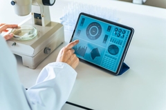 A person touches a screen while looking at ingredients under a microscope.