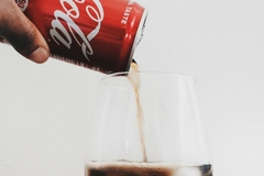 A hand pouring a can of Coke into a glass.