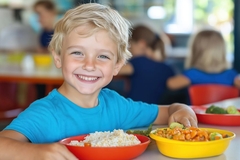 Image young boy is smiling and eating food at school lunch