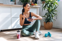 Image Fit woman in gym wear sits on her workout mat eating healthy meal