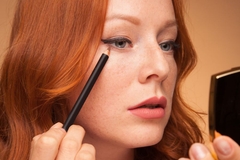 Image Woman applying eyeliner pencil while looking in compact mirror