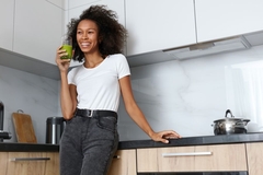 Image Woman drinking a green beverage in a kitchen.