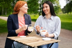 Image two women laughing will eating yogurt from a paper based cup