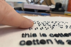Image A finger touching a piece of fabric with small letters and braille