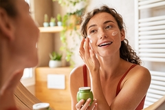 Woman applying skin cream in mirror.