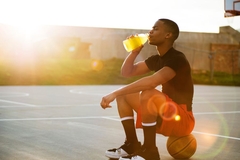 Image Man drinks as he sits on a basketball
