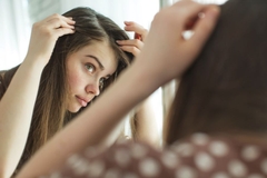 Image A woman looking at her scalp in the mirror.