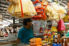 Image A person standing in a market stand that has many plastic bags