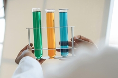 Hands holding three test tubes with liquids of different colors.