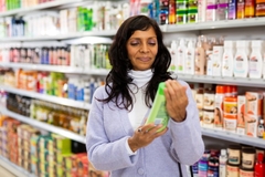 A woman looking at a bottle in the body care aisle.