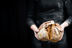 Image A baker cracking open a round loaf of dark bread.