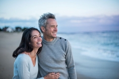 A very happy and satisfied looking older couple stare at the horizon on the beach while smiling.