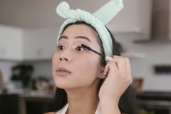 Image A woman applying mascara and wearng a fluffy headband.