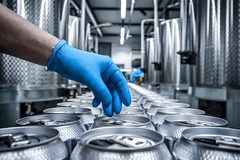 Blue gloved hand inspects silver cans in industrial workshop setting