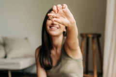 Image A woman happily holds up an omega-3 supplement while sitting on a couch.