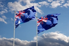 Australia and New Zealand's flags flying side by side on poles on a clear and sunny day.