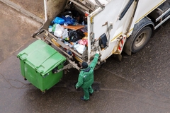 Image A person in green overalls putting garbage into a garbage truck