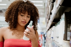 Image A woman looking at a bottle on a shelf in a store.