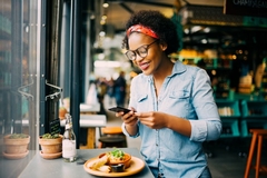 Image A woman smiles while taking a picture of her food in a resteraunt.