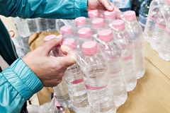 Image A person holding a box of mineral water bottles.
