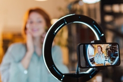 Image A woman putting a roller on her face as seen through her phone in front of a ring light.