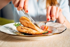 Image A person cutting up cooked chicken breast on a plate.