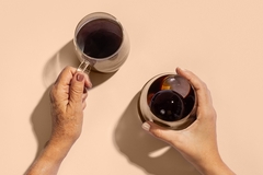 two hands with transparent coffee mugs against a peach background
