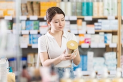 Image A woman reads the label on a supplement in a health food store.
