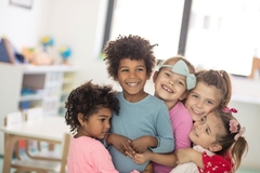 Image Several children hugging and smiling in room filled with toys.