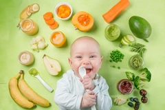Image smiling baby holding spoon surrounded by fruit and veggies