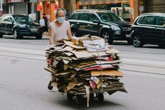 Image A person wearing a face mask pushing a cart full of cardboard.
