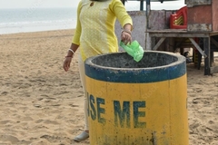 Image woman throwing plastic bag in bin on beach