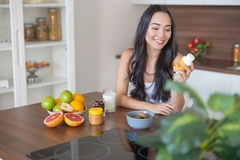 Image A young woman taking a nutritional supplement at breakfast.