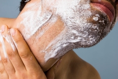 A man touching his neck with shaving cream on it.