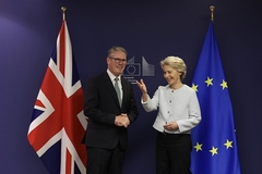 a man and a woman in professional clothes standing in front of UK and EU flags