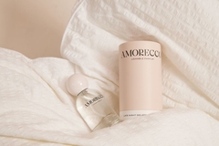 Amorecco's perfume sitting on bed sheets.