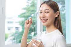 woman smiles with supplement and glass of water