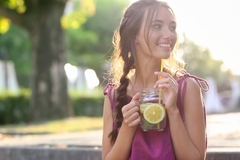 Image Woman drinking citrus beverage outside in the sunshine.