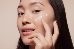 Asian woman applying skin care product.