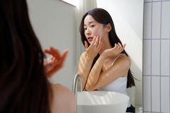 Image A woman touching her cheek while looking in the mirror.