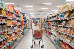 Image Shopping cart stands in aisle between shelves full of products in supermarket