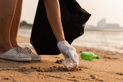 A person picking up a plastic bottle on a beach.