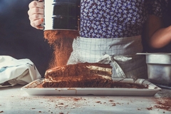 Image a person sifting cocoa powder over a cake