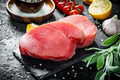 Image Raw tuna fillet on a stone board with salvia and lemon.