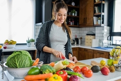 Image A woman chops up vegetables on a cutting board that rests on a countertop that is covered with vegetables and fruits.